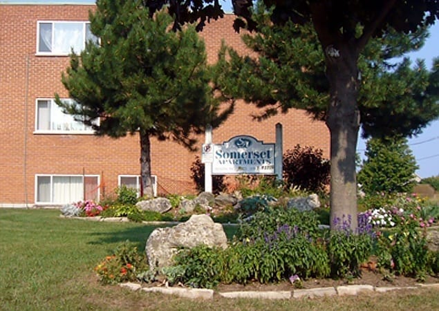 Sign for Somerset Apartments standing in a garden underneath pine trees