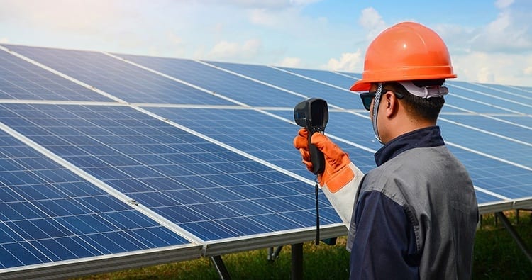 Worker uses a heat gun on solar panels to determine their temperature