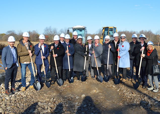 A group of people standing at a construction site, posing with shovels dug into the soil.