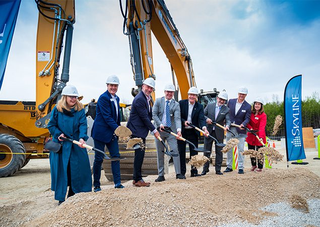 Smiling people with groundbreaking shovels and hard hats at a construction site.